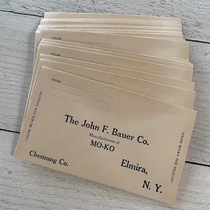 May include: A stack of vintage cream-colored cards with the text "The John F. Bauer Co. Manufacturers of MO-KO" printed in black. The cards also include the text "Chemung Co., Elmira, N.Y." and "Drink MO-KO for Health."