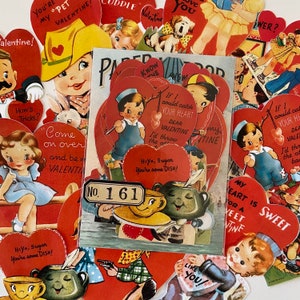 Op de afbeelding: Een verzameling vintage Valentijnskaarten en -ephemera. De kaarten bevatten hartvormen, illustraties van kinderen en romantische zinnen. Een centraal stuk is een papieren advertentie met het nummer 161.