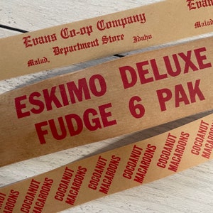 May include: Close-up of three vintage food product labels. The top label reads "Evans Co-op Company, Department Store, Idaho." The middle label says "Eskimo Deluxe Fudge 6 Pak." The bottom label repeats "Cocoanut Macaroons."