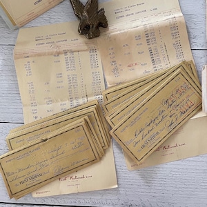 May include: A collection of vintage bank checks and financial documents, including a ledger and checks from The First National Bank of Celina, Ohio. A brass eagle paper clip rests on top.