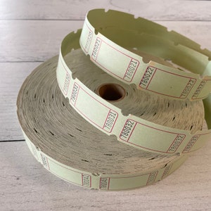 Puede incluir: Un rollo de boletos verde pálido vintage con bordes rojos y numeración secuencial. Varias tiras de boletos están desenrolladas, mostrando los números 780020 a 780033. Los boletos están sobre una superficie de madera blanca.