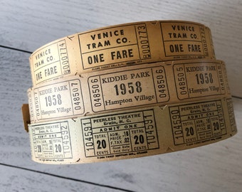 May include: A stack of vintage paper tickets with printed text. The tickets are tan with black ink, featuring text like "Venice Tram Co. One Fare" and "Kiddie Park 1958." The tickets are rolled up, showing their edges.