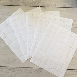 Peut inclure: Plusieurs feuilles de papier blanc, chacune avec un motif quadrillé de lignes pointillées. Les feuilles sont disposées en éventail, leurs bords se chevauchant. Le papier a un aspect propre et net.