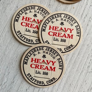 May include: Three vintage cream bottle caps. Each cap is circular with a cream-colored background and black and red text. The text reads "MAPLESHADE JERSEY DAIRY" around the edge, with "HEAVY CREAM" and "Lic. 350" in the center.