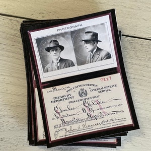 Op de afbeelding: Een stapel kaarten in vintage-stijl met zwart-witfoto's van een man in pak en hoed. De kaarten bevatten ook tekst van het Amerikaanse ministerie van Financi&euml;n en de Internal Revenue Service, met het woord "PHOTOGRAPH" bovenaan.