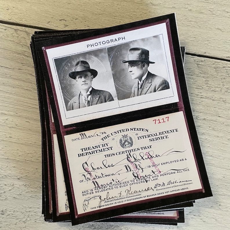 Op de afbeelding: Een stapel kaarten in vintage-stijl met zwart-witfoto's van een man in pak en hoed. De kaarten bevatten ook tekst van het Amerikaanse ministerie van Financi&euml;n en de Internal Revenue Service, met het woord "PHOTOGRAPH" bovenaan.