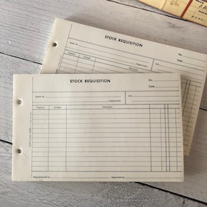 May include: Two vintage stock requisition forms. Each form is white with black text and horizontal lines for filling in information. The forms are labelled "STOCK REQUISITION" at the top and include fields for quantity, number, and description. The forms are hole-punched for binding.