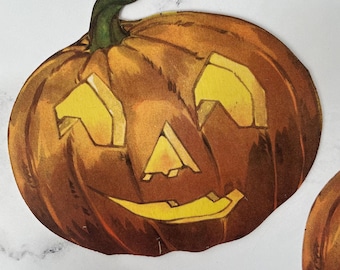 May include: A vintage-style, orange pumpkin with a carved face, featuring triangular eyes and a toothy grin. The pumpkin has a green stem and is likely a Halloween decoration.