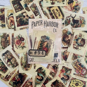 May include: A collection of vintage-style ephemera, including labels, cards, and tags. The designs feature illustrations of roses, portraits, and advertisements. A package of stickers with the text "PAPER HARBOR CO." and "No. #94" is in the center.