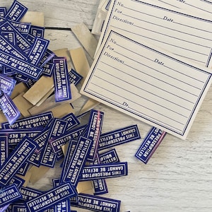 May include: A collection of blue and white stickers with the text "THIS PRESCRIPTION CANNOT BE REFILLED" scattered around prescription forms. The forms have lines for patient information and the doctor's signature.