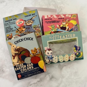 May include: A selection of vintage Easter egg colour kits, featuring illustrations of bunnies, chicks, and decorated eggs. The boxes display text such as "Easter Egg Colour Kit" and "Happy Easter".