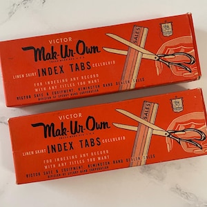 Könnte beinhalten: Zwei orangefarbene Vintage-Boxen mit "Victor Mak-Ur-Own Index Tabs Celluloid" mit schwarzem Text und Illustrationen. Die Boxen zeigen eine Schere, die Indexkarten schneidet, und den Text "Sales". Die Boxen dienen zum Indizieren beliebiger Datensätze.