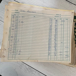 May include: A stack of vintage ledger sheets with handwritten entries. The top sheet is labeled "Thomas Armstrong" and includes columns for dates, items, credits, and balances. The paper has a yellowed hue, with visible hole punches along the left edge.