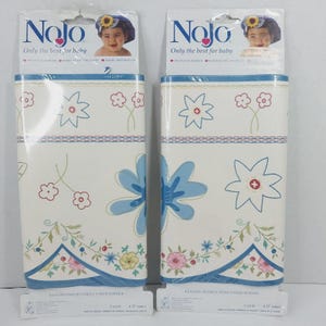 May include: Two rolls of baby border wallpaper with a floral design. The wallpaper features blue, pink, and yellow flowers on a cream background. The top of the packaging has the brand name "Nojo" and the text "Only the best for baby".