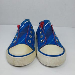 Op de afbeelding: Een paar blauwe canvas sneakers met witte rubberen zolen en neuzen. De sneakers hebben een gestreept ontwerp aan de zijkanten en rode accenten rond de kraag. Ze hebben metalen veterogen.