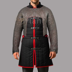 May include: A medieval-style chainmail shirt with long sleeves, worn over a black padded gambeson. The gambeson features red trim and straps with buckles. The garment is designed for historical reenactment or costume use.