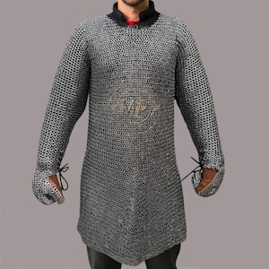 Puede incluir: Una camisa de cota de malla plateada con mangas largas y cuello alto. La camisa tiene un cuello redondo con un acento rojo y guantes de cuero. La cota de malla está hecha de pequeños anillos de metal entrelazados.