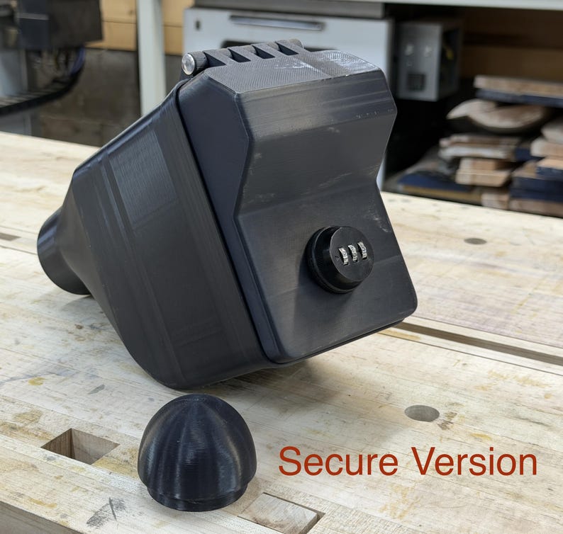 Puede incluir: Un contenedor negro rectangular con cerradura de combinaci&oacute;n y tapa redondeada extra&iacute;ble. El contenedor tiene una superficie texturizada y una extensi&oacute;n cil&iacute;ndrica en un lado. El texto "Secure Version" est&aacute; impreso en rojo.