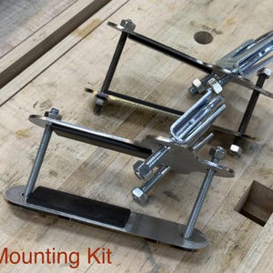 Puede incluir: Un kit de montaje met&aacute;lico con soportes plateados, pernos y almohadillas de goma negra. El kit incluye m&uacute;ltiples piezas, ensambladas con tuercas y pernos, y est&aacute; dise&ntilde;ado para un montaje seguro. El texto "Mounting Kit" es visible.