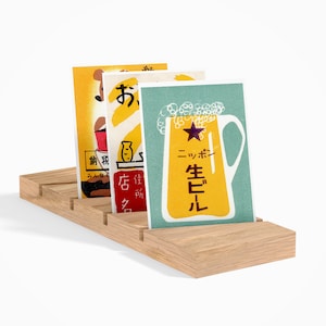 May include: Three vintage Japanese postcards featuring illustrations of a beer mug, a fish, and a bottle. The postcards are displayed on a wooden stand with slots for holding cards.