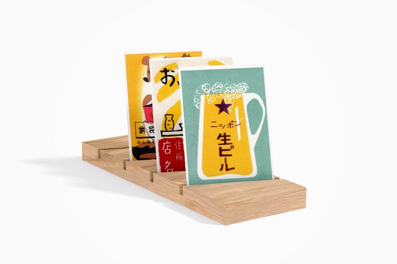 May include: Three vintage Japanese postcards featuring illustrations of a beer mug, a fish, and a bottle. The postcards are displayed on a wooden stand with slots for holding cards.