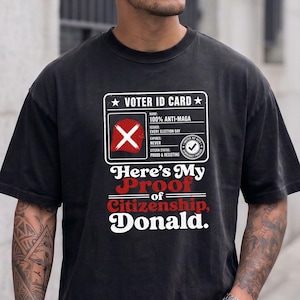 Peut inclure: Un t-shirt noir à manches courtes avec un graphique blanc représentant une carte d'électeur. La carte affiche le texte 100% ANTI-MAGA, EVERY ELECTION DAY, NEVER et PROUD & RESISTING. Sous la carte, le texte indique Here's My Proof of Citizenship, Donald.