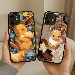 Puede incluir: Dos fundas negras para teléfono con Eevee de Pokémon. Una funda muestra a Eevee durmiendo en un lecho de flores azules y amarillas. La otra funda tiene un diseño de collage con Eevee, chocolate y el texto "there is more to love."