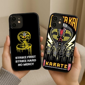 May include: Two black phone cases with Cobra Kai designs. One features a yellow cobra with the text "STRIKE FIRST STRIKE HARD NO MERCY." The other case has a cobra design and the word "KARATE."