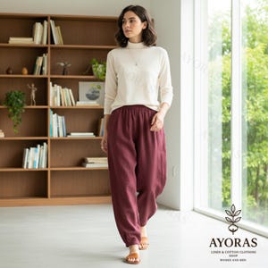 Puede incluir: Una mujer con un jersey de cuello alto color crema y pantalones de lino color burdeos. Los pantalones tienen cintura el&aacute;stica y tobillos fruncidos. La imagen incluye un logotipo que dice "AYORAS LINEN & COTTON CLOTHING SHOP WOMEN AND MEN."