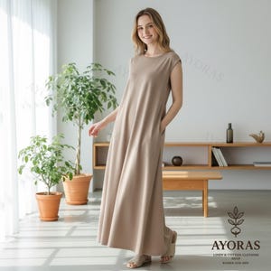 May include: A woman wearing a beige maxi dress with a round neckline and cap sleeves. The dress has pockets and a flowing silhouette. The image includes the text "AYORAS LINEN & COTTON CLOTHING SHOP WOMEN AND MEN".