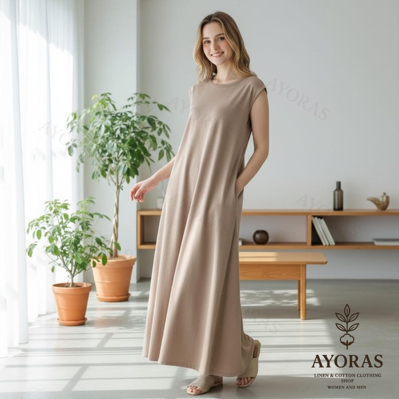 May include: A woman wearing a beige maxi dress with a round neckline and cap sleeves. The dress has pockets and a flowing silhouette. The image includes the text "AYORAS LINEN & COTTON CLOTHING SHOP WOMEN AND MEN".