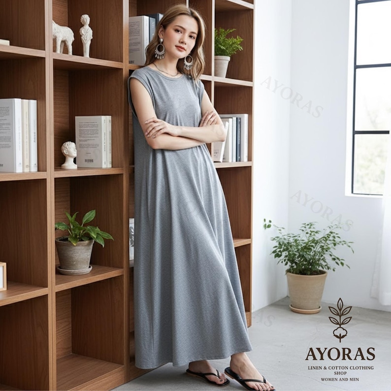 May include: A gray, sleeveless maxi dress with a round neckline. The dress is made of a soft fabric and falls to the ankles. The image also shows a wooden bookshelf and the text "AYORAS LINEN & COTTON CLOTHING SHOP WOMEN AND MEN."