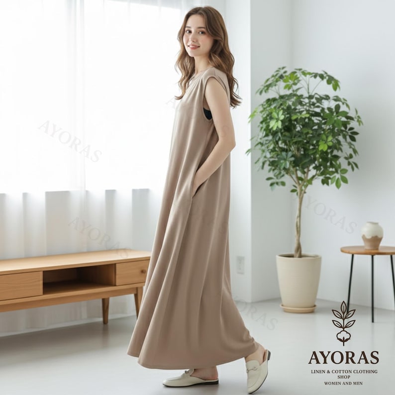 May include: A sleeveless, taupe-colored maxi dress with pockets. The dress is made of a soft, flowing fabric and has a relaxed fit. The dress is part of the AYORAS Linen & Cotton Clothing Shop collection for women and men.