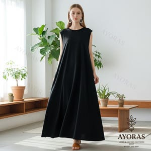 Woman wearing a sleeveless black cotton maxi dress with pockets in a minimalist indoor setting