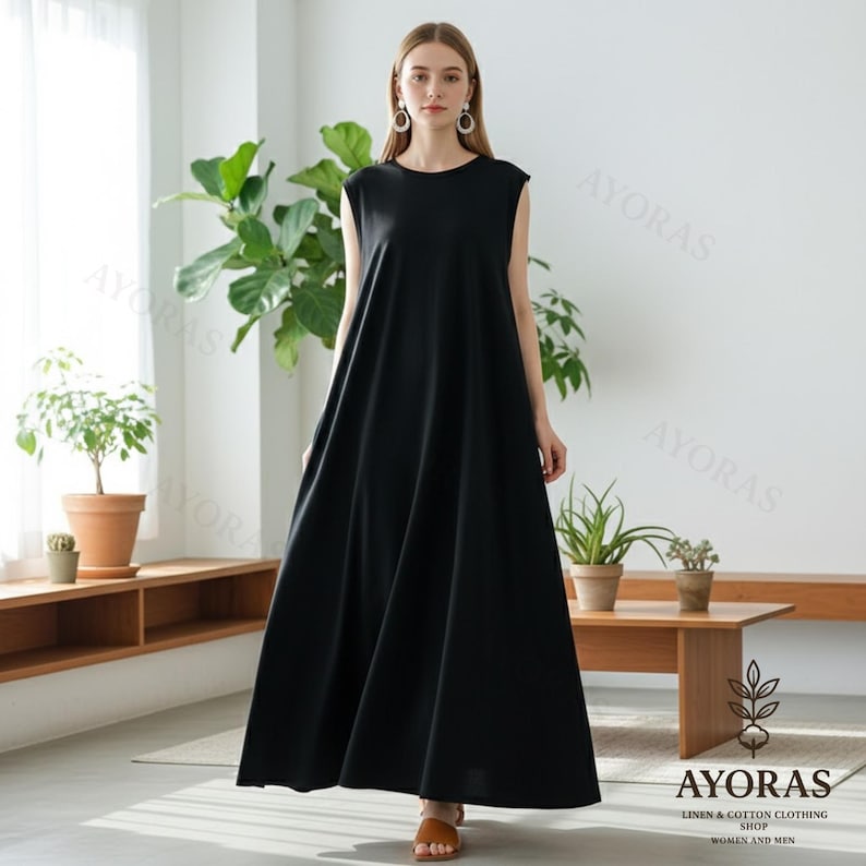 Woman wearing a sleeveless black cotton maxi dress with pockets in a minimalist indoor setting