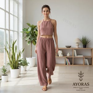 May include: A dusty rose linen halter top and wide-leg pants set. The crop top has a halter neckline, and the pants have a relaxed fit. The set is made of a lightweight, breathable fabric, perfect for warm weather. The logo for AYORAS is visible in the bottom right corner.
