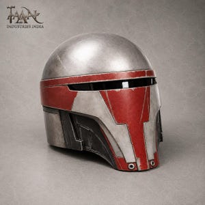 May include: A silver and red helmet with a visor. The helmet has a weathered appearance with red accents on the front and sides. The text "TAAN INDUSTRIES INDIA" is visible in the upper left corner.