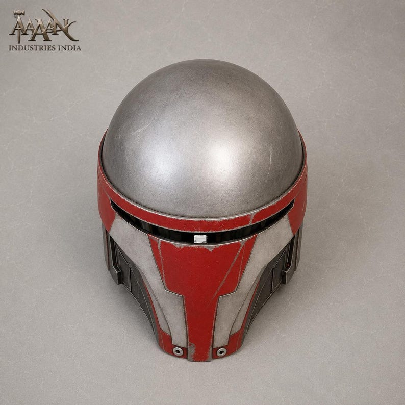 May include: A silver and red helmet with a rounded top and angular faceplate. The helmet features a silver dome and red accents on the face and sides. The design includes black detailing and a small rectangular visor.