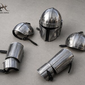 May include: A set of polished metal armor pieces, including a helmet, two shoulder guards, and two arm guards. The helmet has a distinctive T-shaped visor. The armor is silver in color and features black leather straps.