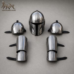 May include: A set of metallic silver Mandalorian armor pieces, including a helmet, two shoulder caps, and two arm guards. The helmet has a T-shaped visor. The arm guards and shoulder caps have black straps. The armor is displayed on a gray surface.