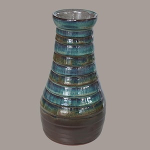 Könnte beinhalten: Eine Keramikvase mit verjüngtem Hals und breitem Boden, die eine Reihe horizontaler Rillen entlang des Körpers aufweist. Die Glasur verläuft von einem dunklen Braun am Boden zu einem leuchtenden Blau- und Türkisverlauf am oberen Rand.