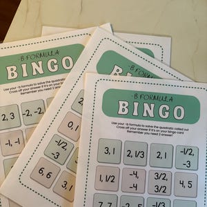 May include: A stack of white paper bingo cards with a green and white border. Each card features the words "-B FORMULA BINGO" at the top. The bingo cards have numbers and fractions in small squares, designed for a maths game.