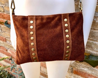 May include: A brown suede crossbody bag with a rectangular shape. The bag features vertical brown leather straps on each side, adorned with evenly spaced gold-colored rivets. The bag has a chain strap and gold-colored hardware.