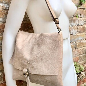 May include: A light brown leather shoulder bag with a flap closure and a buckle. The bag has a long strap and is made of a soft, textured leather.