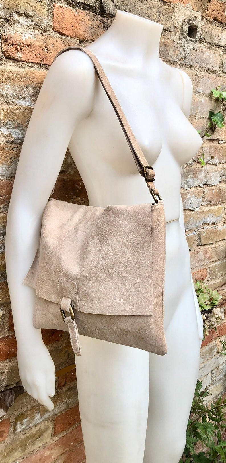 May include: A light brown leather shoulder bag with a flap closure and a buckle. The bag has a long strap and is made of a soft, textured leather.