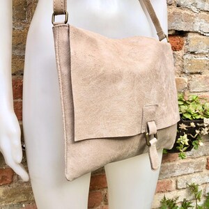 May include: A light beige leather shoulder bag with a flap closure and a buckle detail. The bag has a long strap and is made of a soft, textured leather.