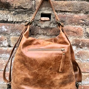 Op de afbeelding: Een bruine leren rugzak met een ritsvak en verstelbare schouderbanden. De tas heeft een verweerde, vintage look.
