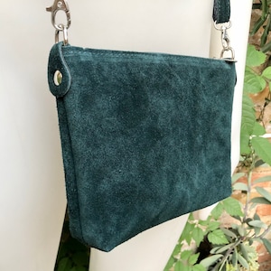 May include: A dark green suede crossbody bag with a silver chain strap and a silver clasp.