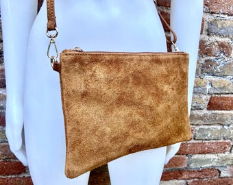 May include: A brown suede crossbody bag with a zipper closure and a long, adjustable strap. The bag is rectangular and has a soft, textured appearance. The strap is attached with silver-colored metal hardware.