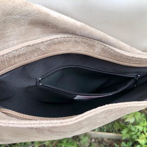 May include: A beige suede bag with a black zippered pocket inside. The bag is open and the inside is visible.